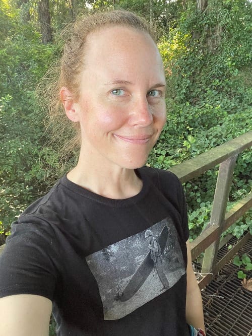 Smiling white woman in black shirt with green forest background